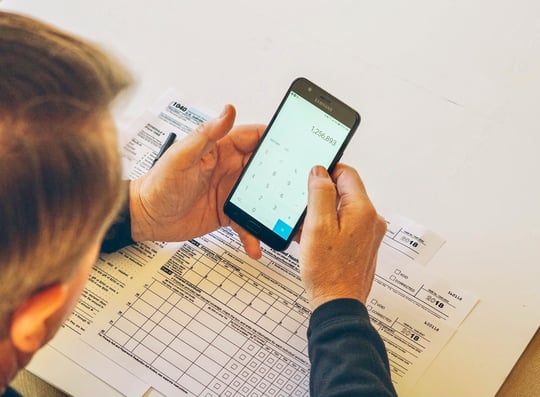 overhead-view-of-a-man-completing-annual-federal-tax-forms-and-holding-a-calculator_t20_980lm8